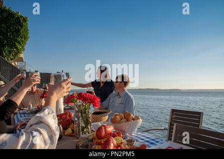 Group of friends raising glasses at a seafood dinner seaside in late afternoon sun. Stock Photo