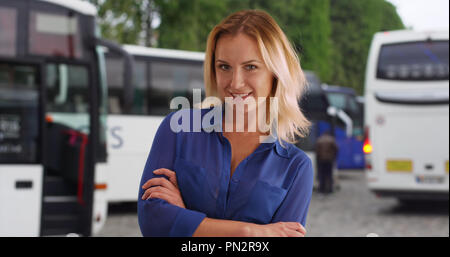 Confident young woman in blue shirt posing for camera near tour buses outside Stock Photo