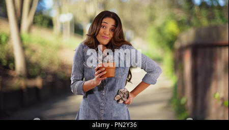 Friendly Hispanic woman standing in park on sunny day holding out small plant Stock Photo