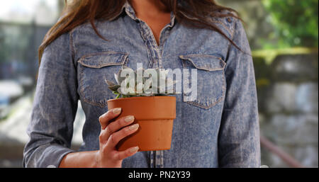 Close up of Hispanic woman in casual shirt holding cactus outside on sunny day Stock Photo