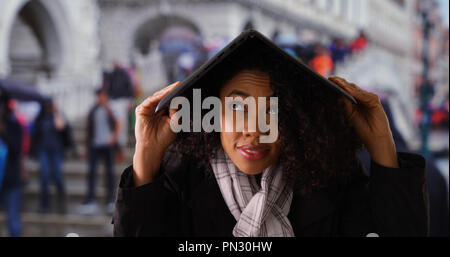 Woman using laptop computer to protect herself from rain in Venice Stock Photo