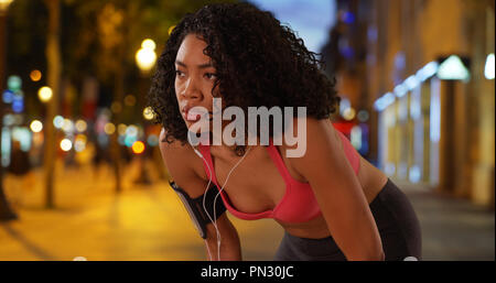Black woman runner taking break while on a run in the city at night Stock Photo