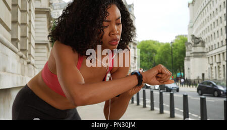 African American woman runner checking fitness tracker in urban setting Stock Photo