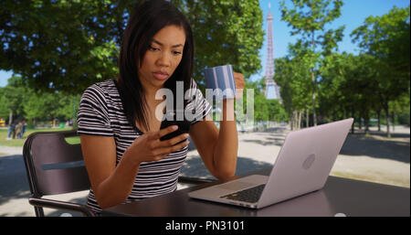 Black woman texting on smartphone while drinking coffee in park in Paris France Stock Photo