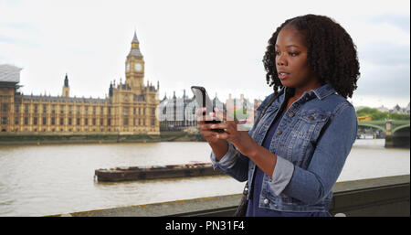 Pretty black woman traveling in London looking at map app on cell phone Stock Photo