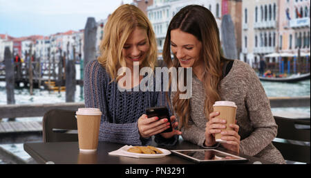 Couple of attractive girls sitting and using on smart phone by Venetian canal Stock Photo