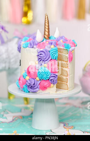 Sliced multilayer unicorn cake on cake stand at the little girl birthday party. Stock Photo