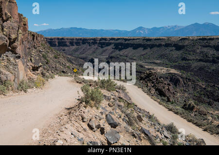 Dangerous dirt road at the canyon rim of the Rio Grande Gorge near Taos, New Mexico with the Sangre de Cristo mountain range in the background Stock Photo