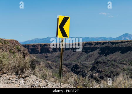 Left turn arrow road sign at a switchback on a road at the canyon rim above the Rio Grande Gorge near Taos, New Mexico Stock Photo