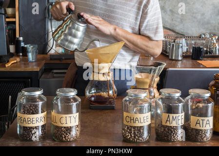 barista holding drip pot and pouring water onto ground coffee beans in the paper filter for brewing drip coffee at the cafe in the morning. coffee dri Stock Photo