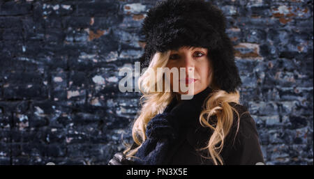 Close up of woman in hat and scarf looking at camera against brick background Stock Photo