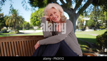 Old woman with happy expression on her face posing on bench on nice day the park Stock Photo