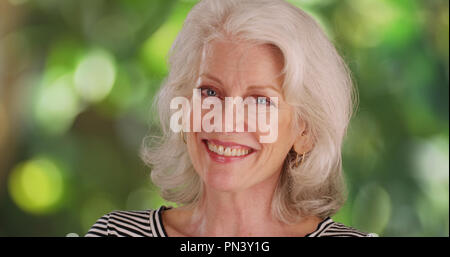 Close-up portrait of old lady smiling at camera in natural outdoor setting Stock Photo