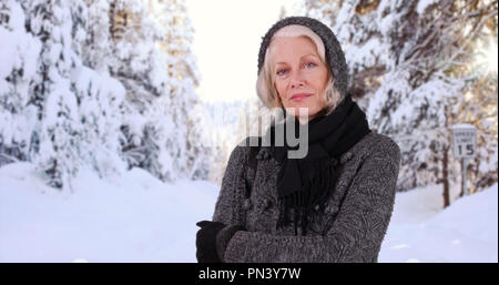 Serious female elder posing with arms crossed outdoors in natural snowy setting Stock Photo