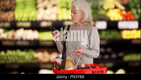 Mature white lady in produce section of grocery store checking smartphone Stock Photo