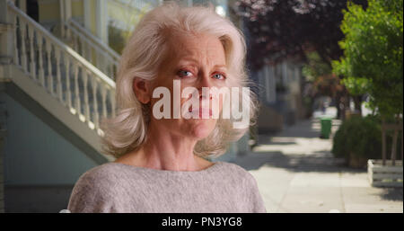 Portrait of female elder standing outside in residential area alone looking sad Stock Photo