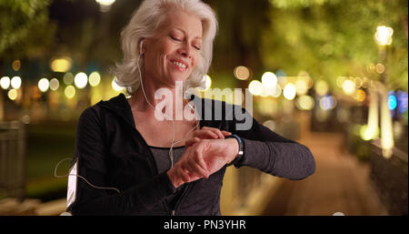 Healthy elderly Caucasian lady checking timer on watch while out on jog at night Stock Photo