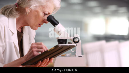 Elderly woman scientist writing on clipboard and looking through microscope Stock Photo