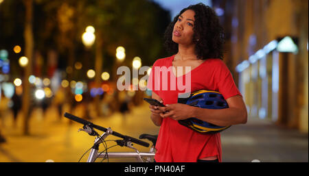 Black woman on bike ride at night checking cell phone map app for direction Stock Photo