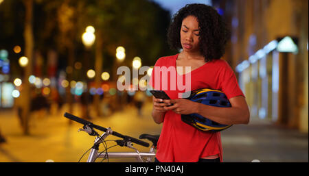 Black woman on bike ride at night checking cell phone map app for direction Stock Photo