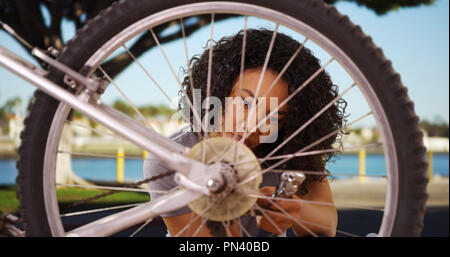 Handy young African-American female working on bicycle wheel outside Stock Photo