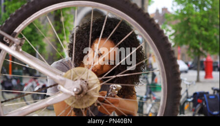 Close up of African woman fixing wheel or tire on bike while in city square Stock Photo