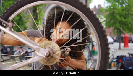 Close up of African woman fixing wheel or tire on bike while in city square Stock Photo