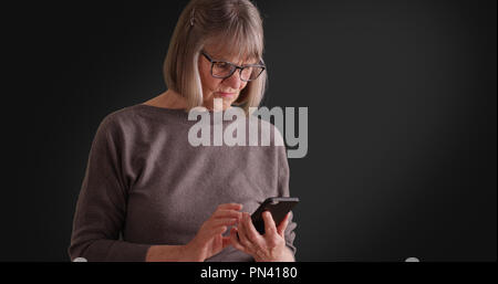 Somber lady reading worrying message on mobile device on dark gray background Stock Photo