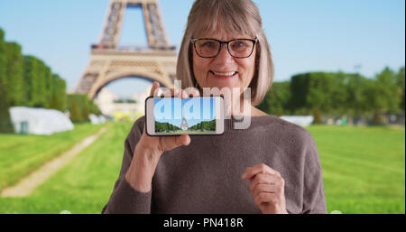 Excited elderly white lady showing off photo she took of Eiffel Tower on phone Stock Photo