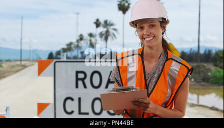 Dolly shot of Female worker in safety vest standing in front of road closed sign Stock Photo