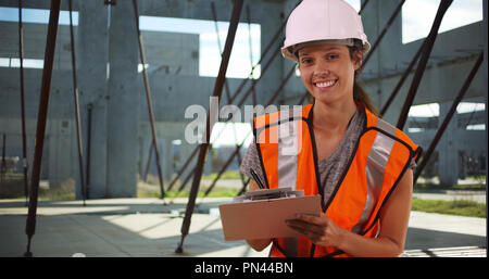 Female construction worker using clipboard and smiling at camera on job site Stock Photo
