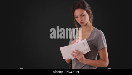 Young Caucasian woman looking through mail she received on dark gray background Stock Photo