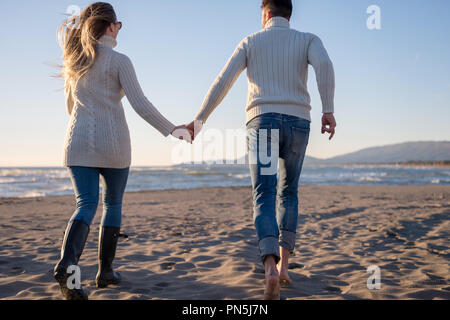 Young couple having fun walking and hugging on beach during autumn sunny day Stock Photo