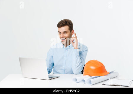 Handsome male engineer is using a notebook for work. He is sitting at the desk and smiling. Copy space on side. Stock Photo
