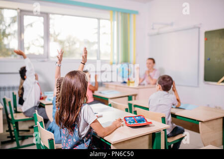 group of school children all raising their hands in the air to answer Stock Photo