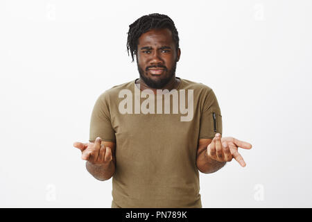Are you kidding me. Frustrated doubtful plump african-american man with beard, pointing with index fingers at camera, frowning and feeling intense, being unsure and questioned over gray wall Stock Photo