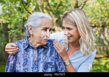 Smiling young caretaker walking with senior lady in the garden Stock Photo