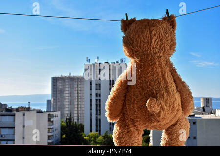 Fuzzy brown teddy bear hanging on a clothesline with high building view Stock Photo