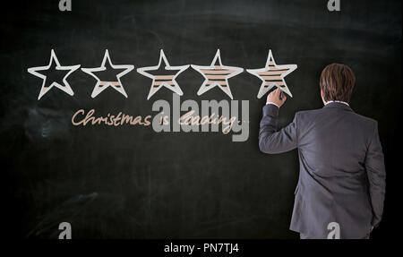 Businessman writes with chalk Christmas is Loading concept on blackboard. Stock Photo