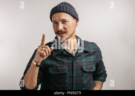 Confident man in knitted hat pointing finger upwards over white background. Stock Photo