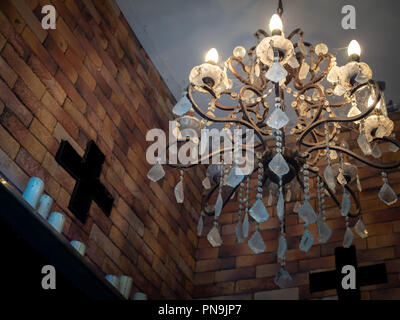 Old vintage crystal chandelier lamp with cobweb on the ceiling with white candles on brick wall with the cross. Stock Photo