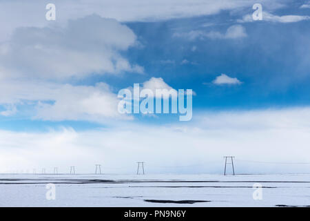 Marching sculptural row of electric power pylons carrying electricity cables across the landscape in South East Iceland Stock Photo