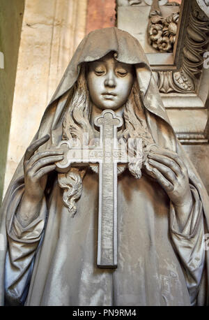 Pictures of a borgeoise realistic style stone sculpture of a girl holding a crucifix on the Poggi Family Tomb. The monumental tombs of the Staglieno M Stock Photo