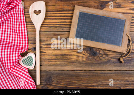 Old rustic slate blackboard with wooden cooking spoon on red white checkered fabric on old wood background with copy space Stock Photo
