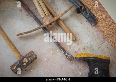 Grungy construction tools such as rubber boot, hammer, crowbar, shovel and digging tool on dirty concrete floor. Exterior construction tool or home fi Stock Photo