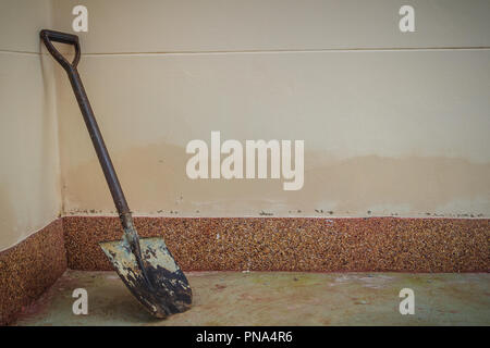 Old and rusty shovel is leaning with grungy wall on dirty concrete floor. Stock Photo
