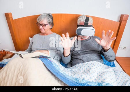 nice beautiful couple caucasian matures man and woman at home in the bedroom stay on the bed during a morning. she read a paper book and he play and u Stock Photo