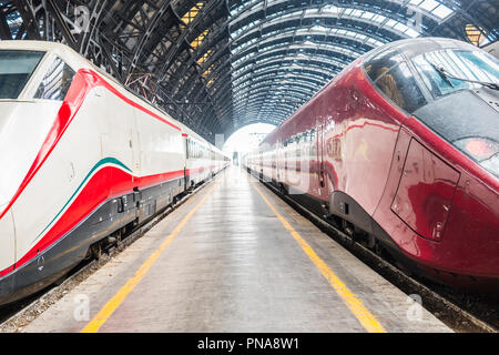 Modern high speed red commuter train at the railway station at sunset. Turning on train headlights. Railroad with vintage toning. Train at railway pla Stock Photo