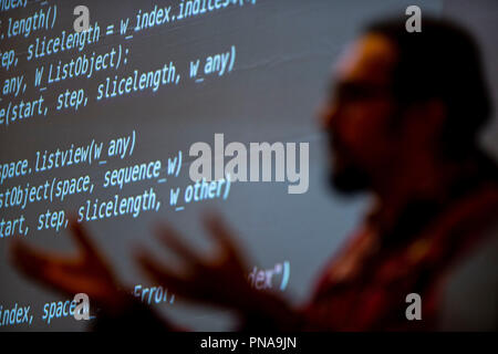 A man delivers a presentation in front of a screen of programmatic code. Stock Photo