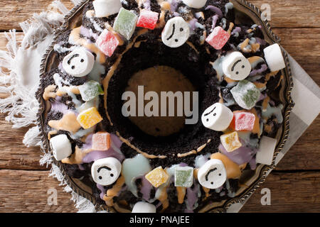 Homemade Halloween chocolate Bundt cake with candied fruits, marshmallow and colorful glaze close-up on the table. Horizontal top view from above Stock Photo